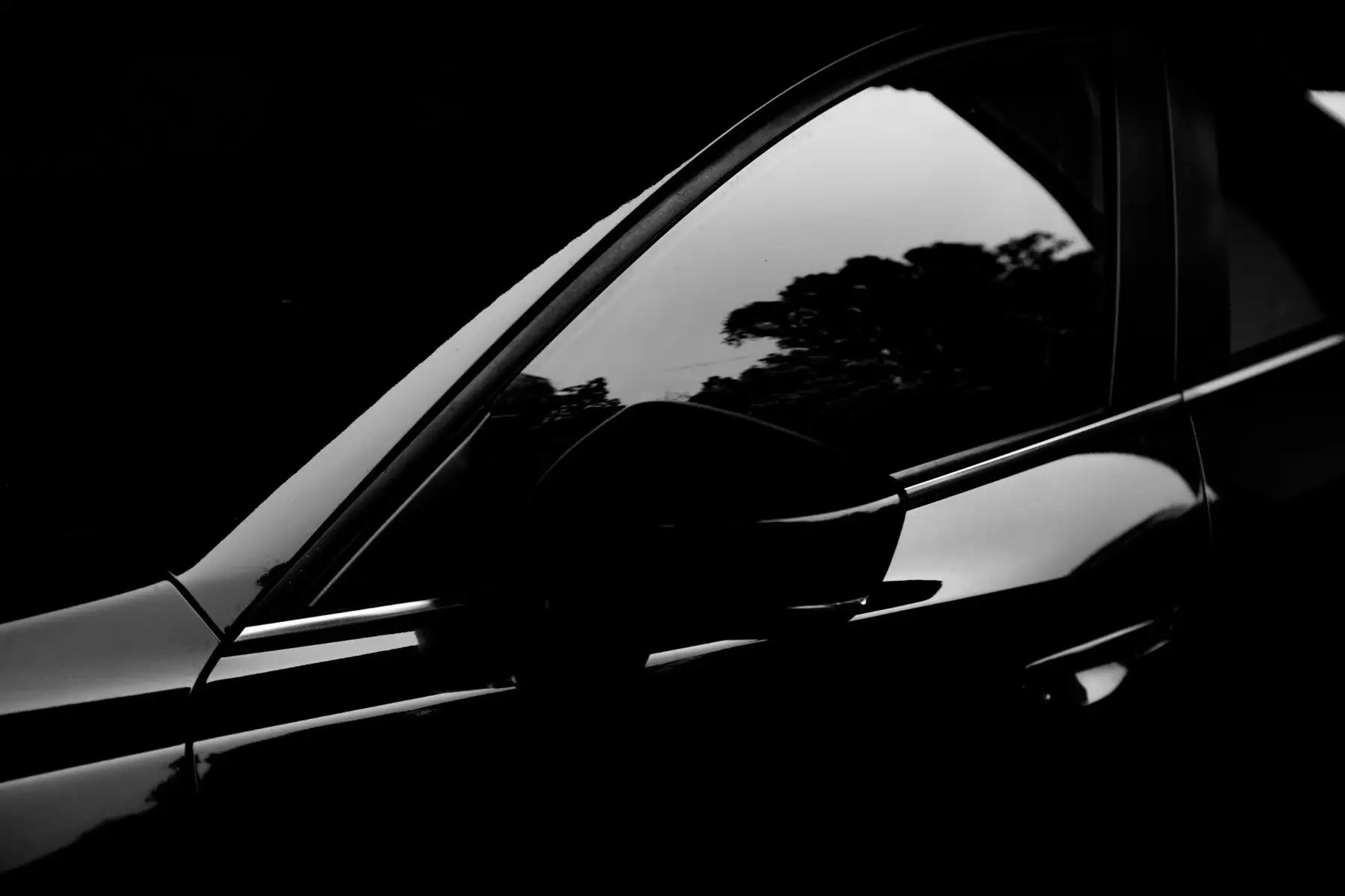 Black car roofline and window in near darkness, one clean line of light along the pillar