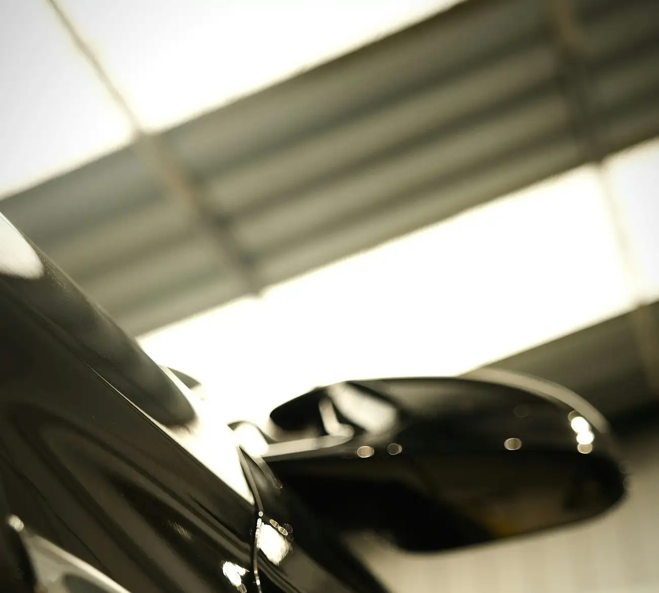 Black sports coupe mirror and door from a low angle, the roof of a garage reflected in the paint