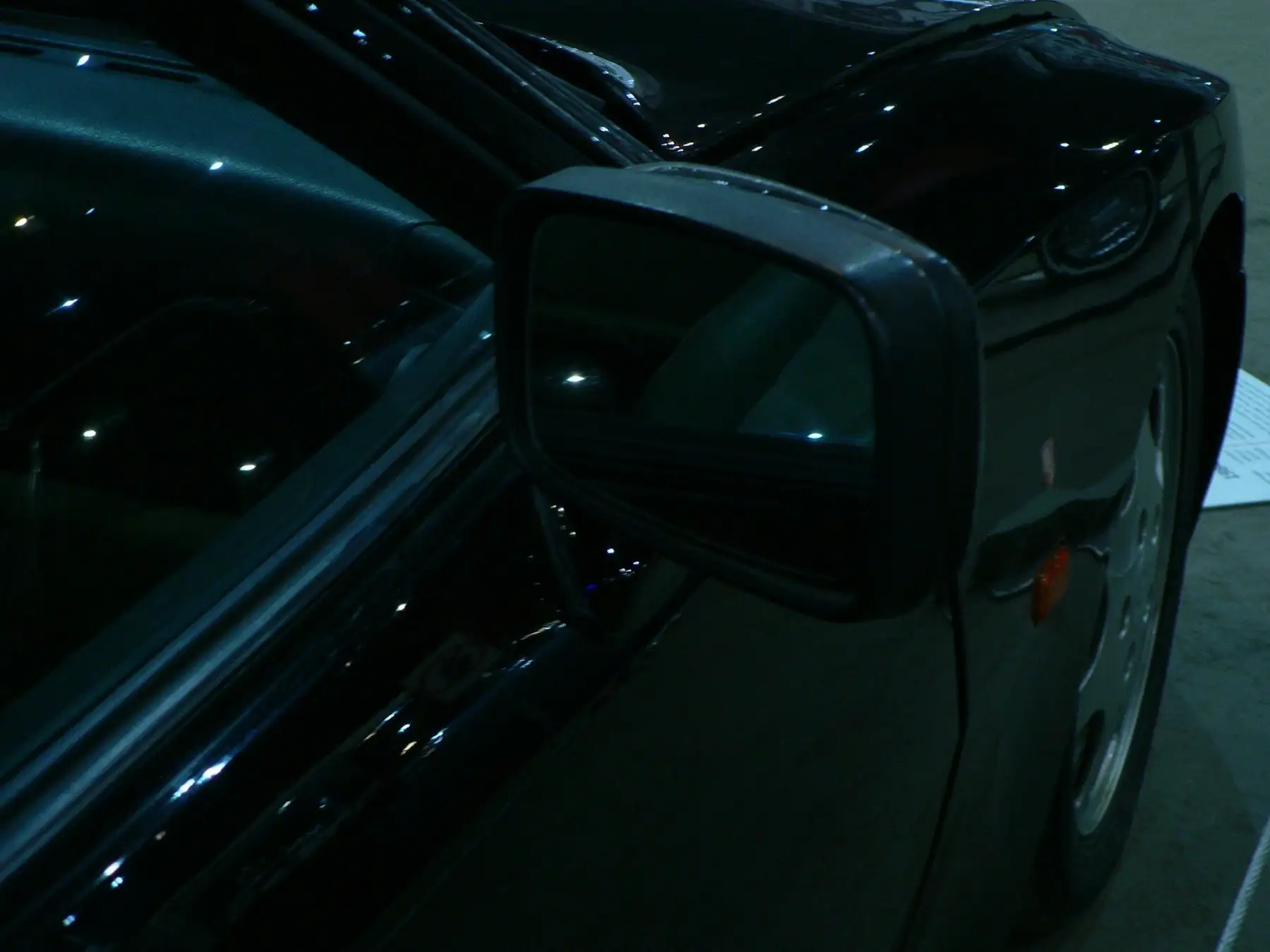 Square door mirror and front wing of a glossy black older SUV, points of light reflected in the paint