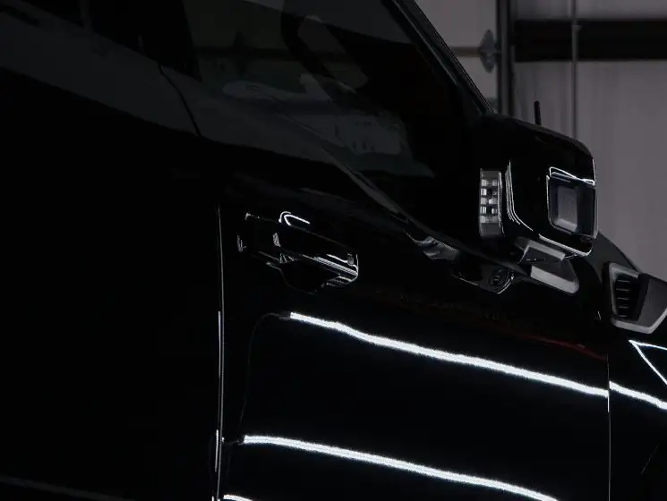 Glossy black pickup door and front fender under shop lights, reflections running straight along the panel