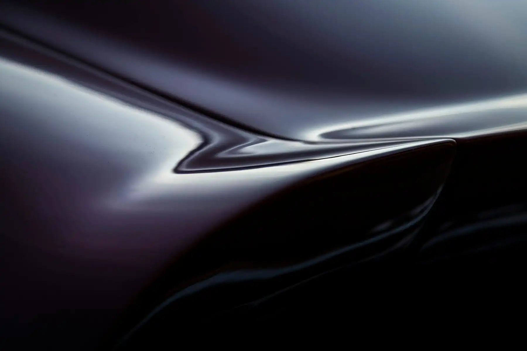 Close-up of a deep black-cherry painted panel curving over a wheel arch, a sharp line of studio light running along the polished clear coat