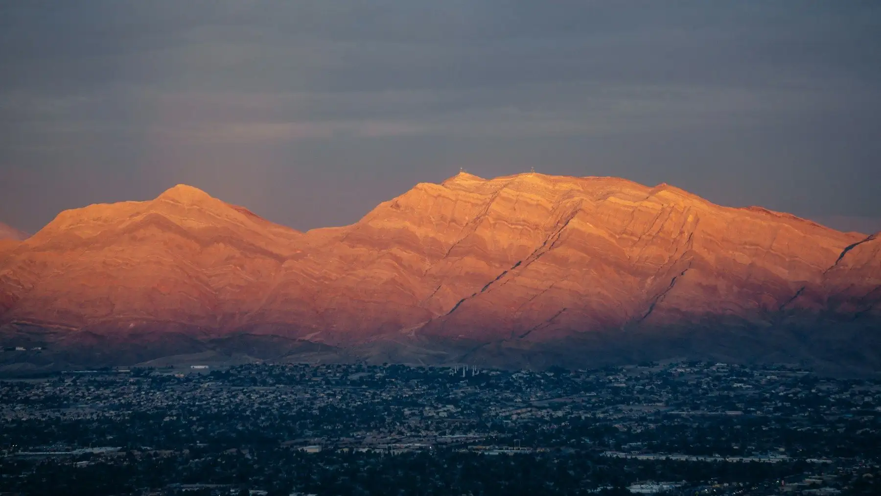 Desert mountain ridge glowing orange in the last sun above the lights of the Las Vegas Valley