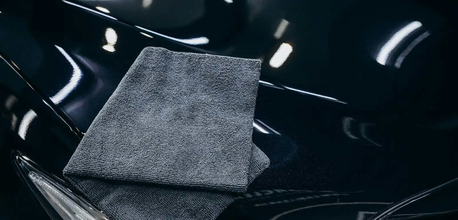 Folded grey microfiber towel resting on the glossy black hood of a freshly coated car