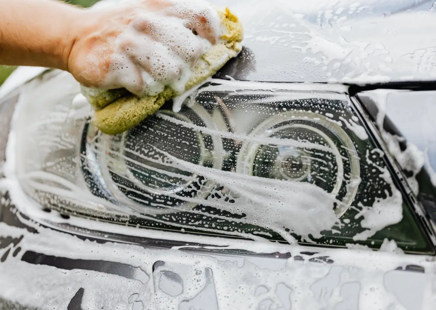 Soapy sponge scrubbing a car headlight lens before restoration