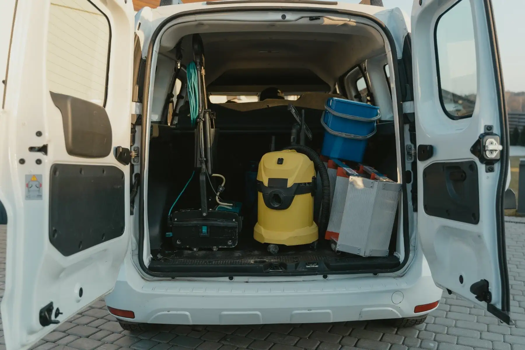 Open back of a white service van loaded with a wet-dry vacuum, a carpet extractor, buckets and supply cases