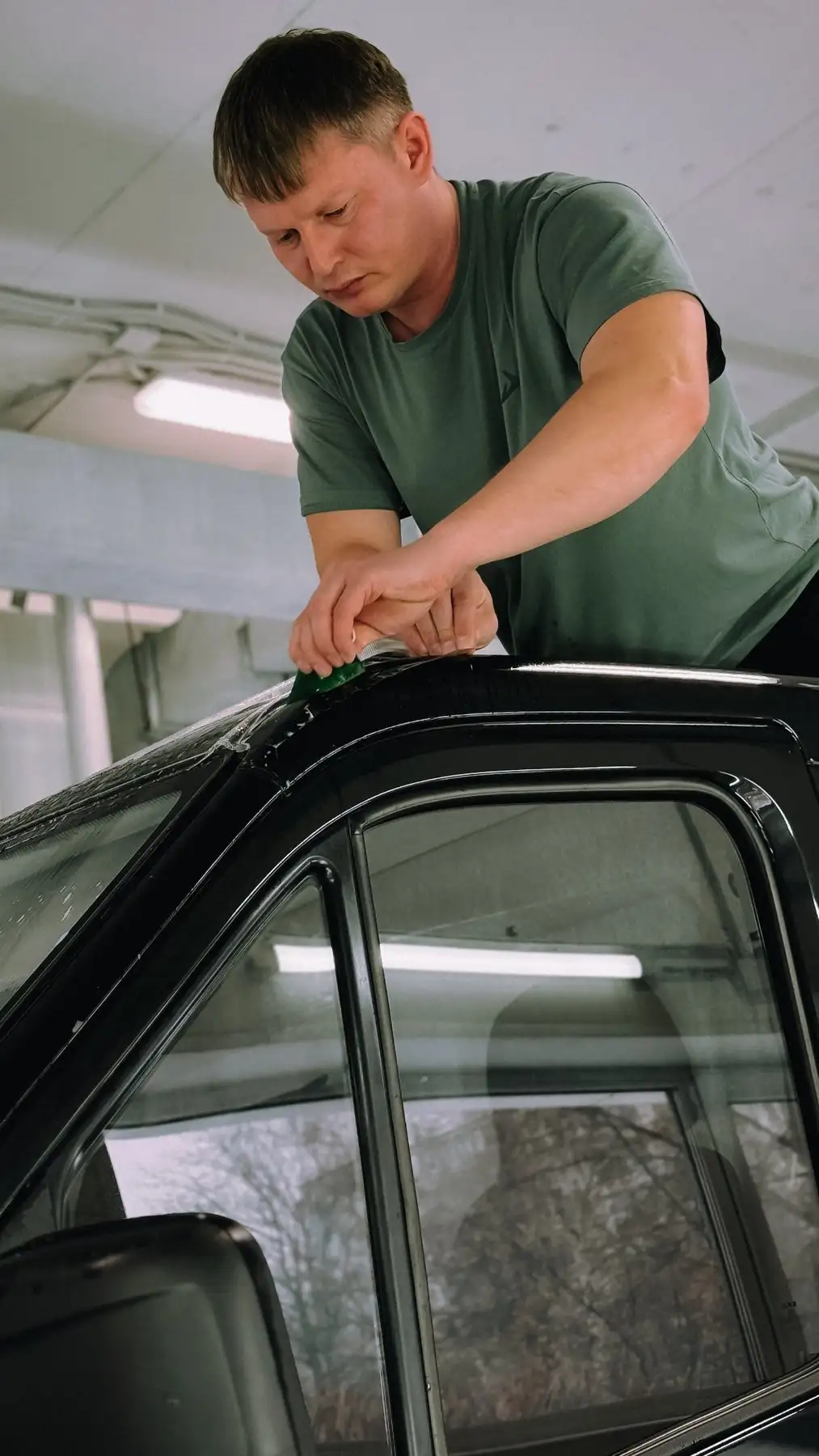 Installer leaning over the roof of a black car, pressing film into the edge of a side window